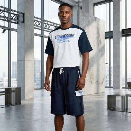 Man in a modern, industrial studio wearing a white and navy "Tennessee Hebrew" t-shirt paired with matching navy cargo shorts.