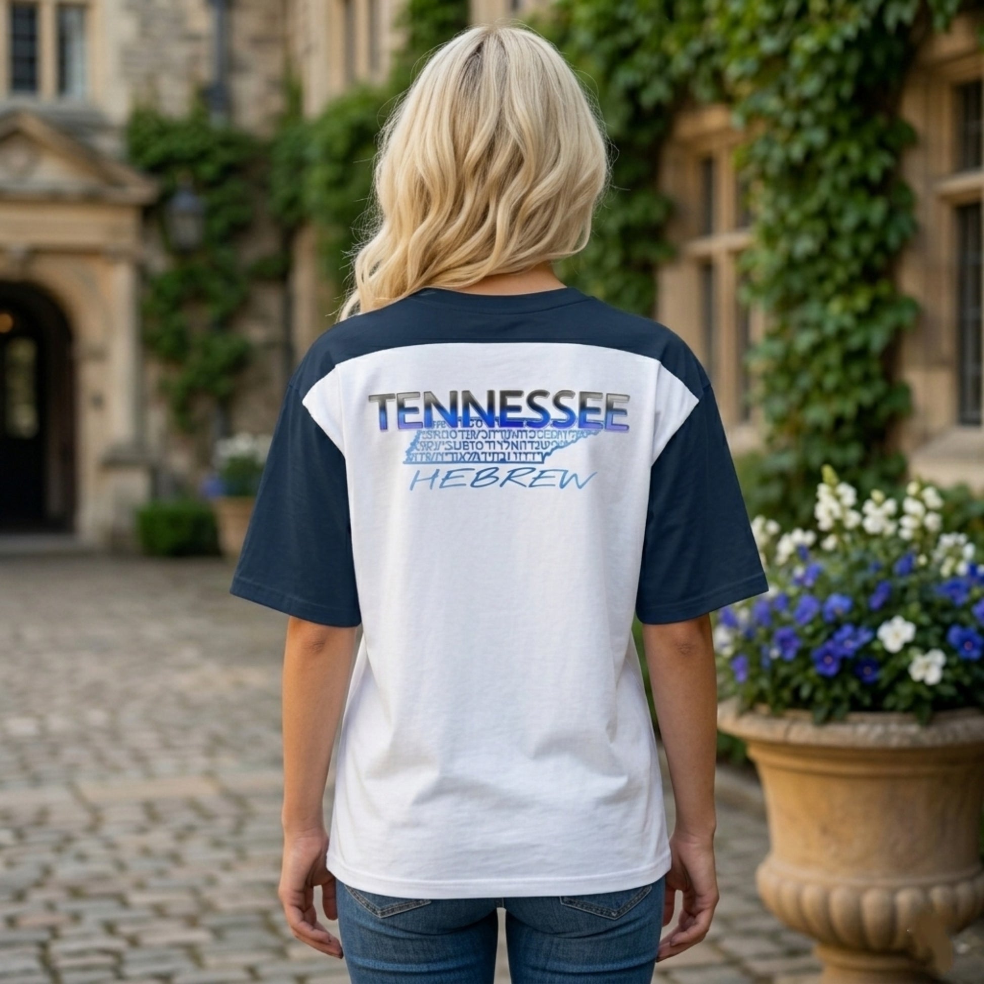 Rear view of a woman wearing a white and navy raglan shirt with a "TENNESSEE HEBREW" graphic on the upper back, standing in a stone courtyard.