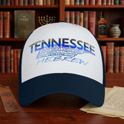 A navy and white trucker hat featuring "TENNESSEE HEBREW" branding sits on a wooden desk in front of a bookshelf with Jewish artifacts and a Jack Daniel's bottle.