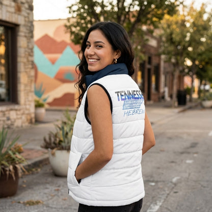 Woman looking over her shoulder on a city street, showcasing a large "Tennessee Hebrew" logo on the back of a white puffer vest.