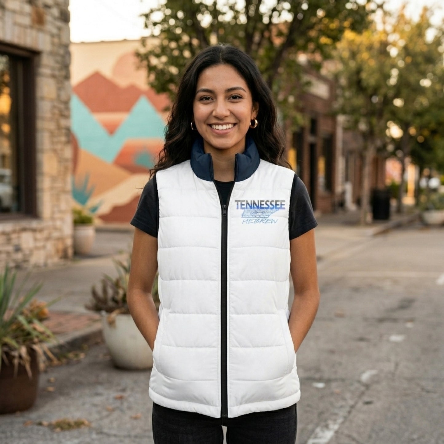 Woman smiling on a city street wearing a white quilted vest with a "Tennessee Hebrew" graphic on the chest.