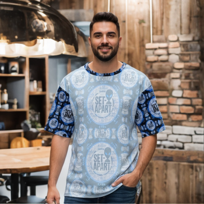 A man with a beard smiles wearing a light blue and navy "SET APART" patterned t-shirt with an alien logo, standing in a rustic room with brick and wood accents.
