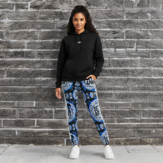 A woman in a black hoodie and blue graphic joggers with white sneakers. She is shown in front view against a stone background.